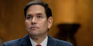 A government official sitting at a hearing with a serious expression