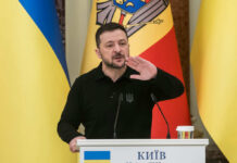 Zelensky’s Purge Sparks Instant Uproar Ukrainian leader speaking at a podium with national flags in the background