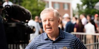 A man in a striped shirt speaking during a media interview at an outdoor event