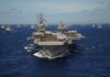 Trump Victory Boast Meets Missile Barrage An aircraft carrier surrounded by various naval ships in the ocean
