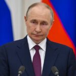 Zelenskyy Dangles Truce; Kremlin Shrugs A serious-looking political figure at a press conference with national flags in the background