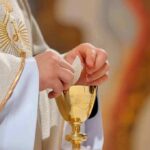 Communion Controversy Erupts at Papal Liturgy Priest holding a communion wafer over a gold chalice