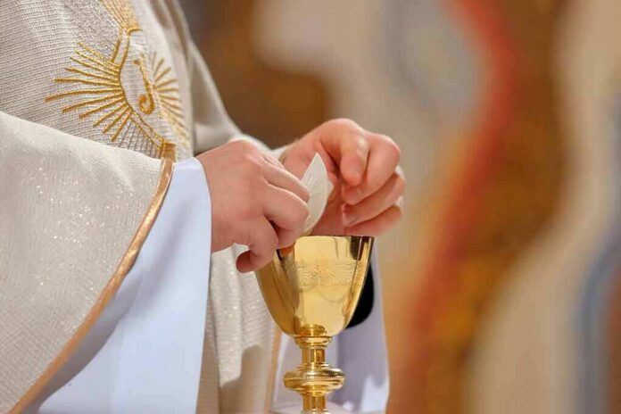 shutterstock_1008001906 Priest holding a communion wafer over a gold chalice