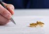 Hand signing a document beside two gold wedding rings