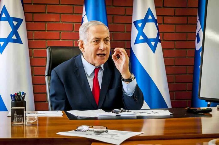 shutterstock_1514247803 man in suit speaking at a desk with Israeli flags behind him