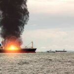 Cargo Ship Downed — Who Pulled Trigger? Cargo ship on fire with thick black smoke at sea