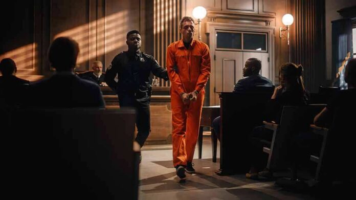 Inmate in orange jumpsuit escorted by officer in courtroom