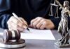 Judge Slams Red Flag Overreach On Kids Judge writing at desk with gavel and Lady Justice statue
