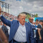 Donald Trump waving while walking through a crowded outdoor event