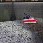 Celebrity Blast Turbocharges Memorial Ban Push American flag on a rainy memorial nameplate.