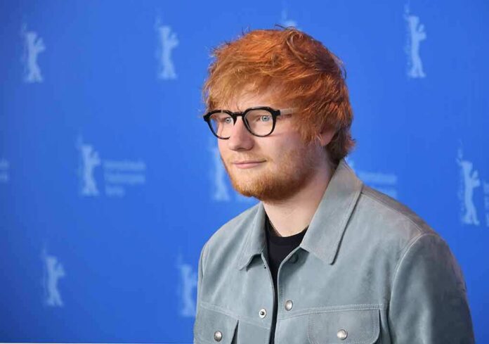 shutterstock_1035592693 Ed Sheeran posing at a photo call against a blue backdrop
