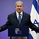 UN Showdown: Netanyahu Taunts City Hall man in suit speaking at a podium with Israeli flag