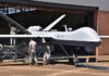 Military drone being serviced by ground crew outside a hangar