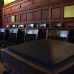 Backlash Forces Juror Underground Empty wooden jury box with numbered chairs