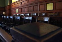 Backlash Forces Juror Underground Empty wooden jury box with numbered chairs