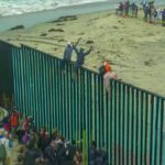 Mass Border Rush Sparks Floating Wall People climbing a tall beachside border fence