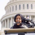 Woman in hijab speaking at podium with microphones