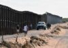 Land Grab Fears Explode in Texas Border fence with patrol vehicles and people walking on a dirt road