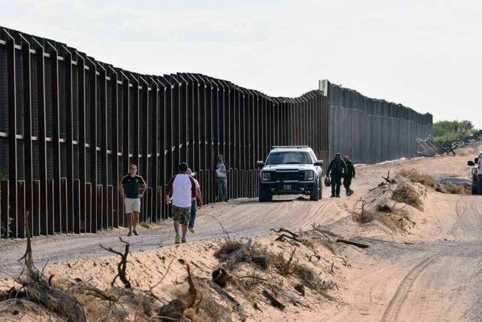 shutterstock_1545833783 Border fence with patrol vehicles and people walking on a dirt road