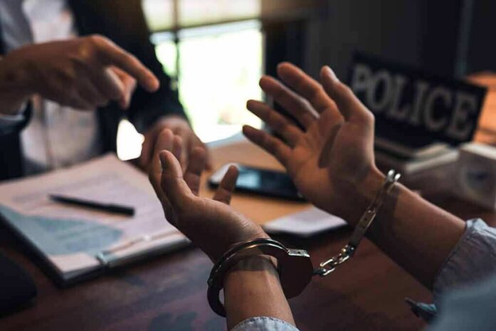 shutterstock_1669066165 Handcuffed person talking with an officer at a desk