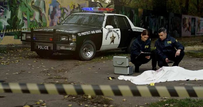 shutterstock_1709493973 Crime scene with police car and two investigators by a covered body