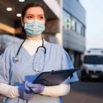 ER Chaos Sparks Miami Outrage Healthcare worker in scrubs wearing mask and gloves holding a clipboard