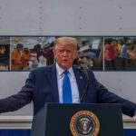 Trump Freezes Strikes — What Did Iran Offer? Donald Trump speaks at a podium with arms outstretched