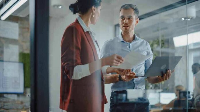 Two colleagues discussing documents in a glass-walled office