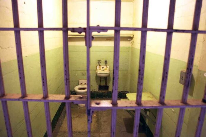 Interior of a prison cell with a toilet, sink, and metal bars