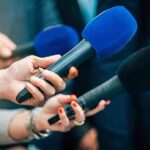 Pricey Tribute? Airport Rename Triggers Backlash Reporters holding colorful microphones