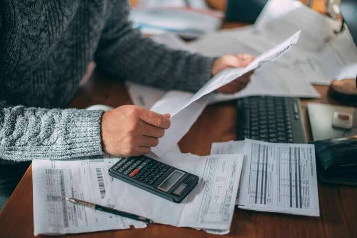 shutterstock_2232534015 Person reviewing bills with calculator at cluttered desk