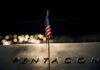 Pentagon Playbook Faces UN Crosshairs Small American flag on a memorial with bokeh lights at night