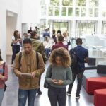 Religious Aid Ban Sparks High Court Gamble Students walking through a bright campus atrium using mobile devices