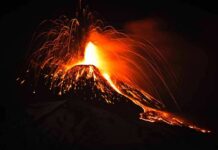 Volcano erupting at night with glowing lava and ash plume