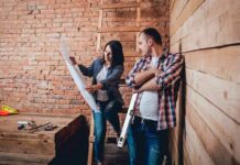 Two people reviewing blueprints in a rustic room under renovation