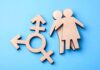 Blue Civil War Erupts Over Trans Messaging Wooden transgender symbol and two human figures on blue background
