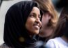 Ilhan Omar smiling in a black hijab at an outdoor event