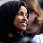 Ilhan Omar smiling in a black hijab at an outdoor event