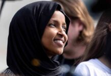 Ilhan Omar smiling in a black hijab at an outdoor event