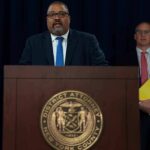 Hochul Overrules DA – James Takes Over Man speaks at podium with New York County District Attorney seal