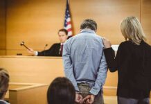 Kentucky Man Faces Trial Over Alleged Trump Threats Defendant in handcuffs stands before a judge in a courtroom