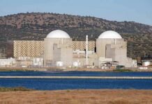 Nuclear power plant with domed structures beside a water body and mountains in the background